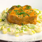 Portrait image of a portion of slow cooker pork loin served with creamed leeks on a white plate with a text overlay