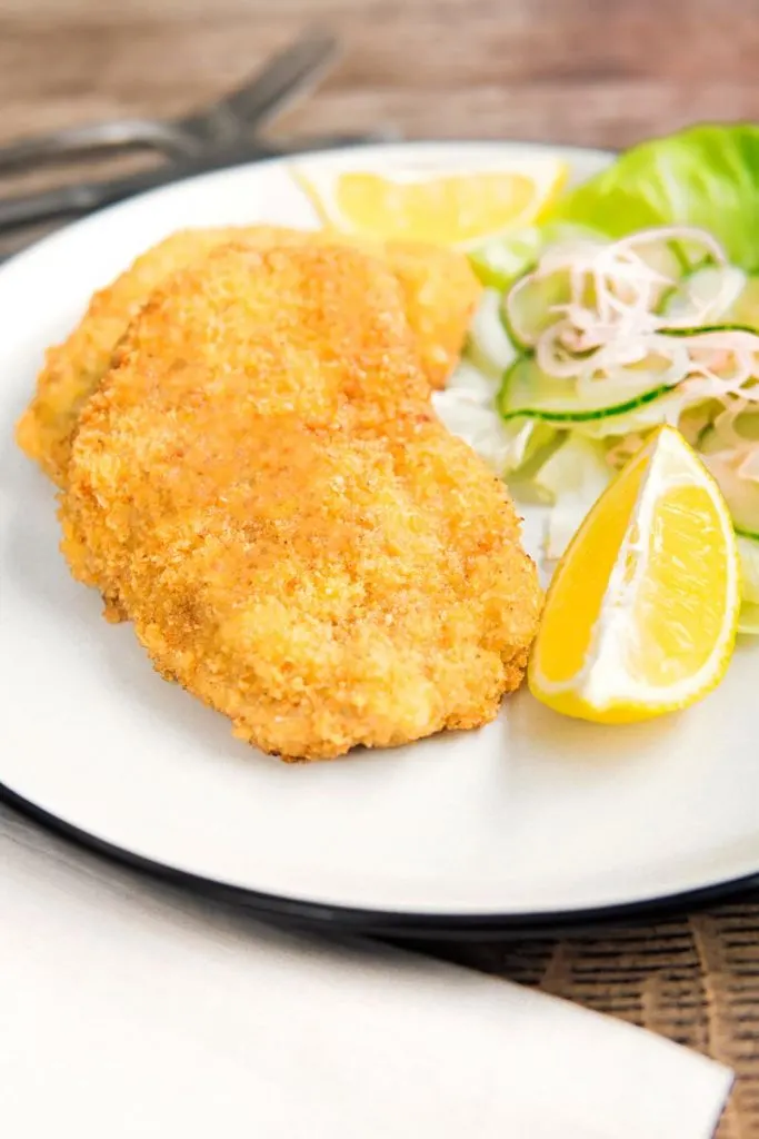 Portrait image of a classic breaded veal Wiener schnitzel served with a classic green salad on a white plate