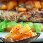 Close up portrait image of a spoonful of chunky apple chutney with an out of focus burger in the background