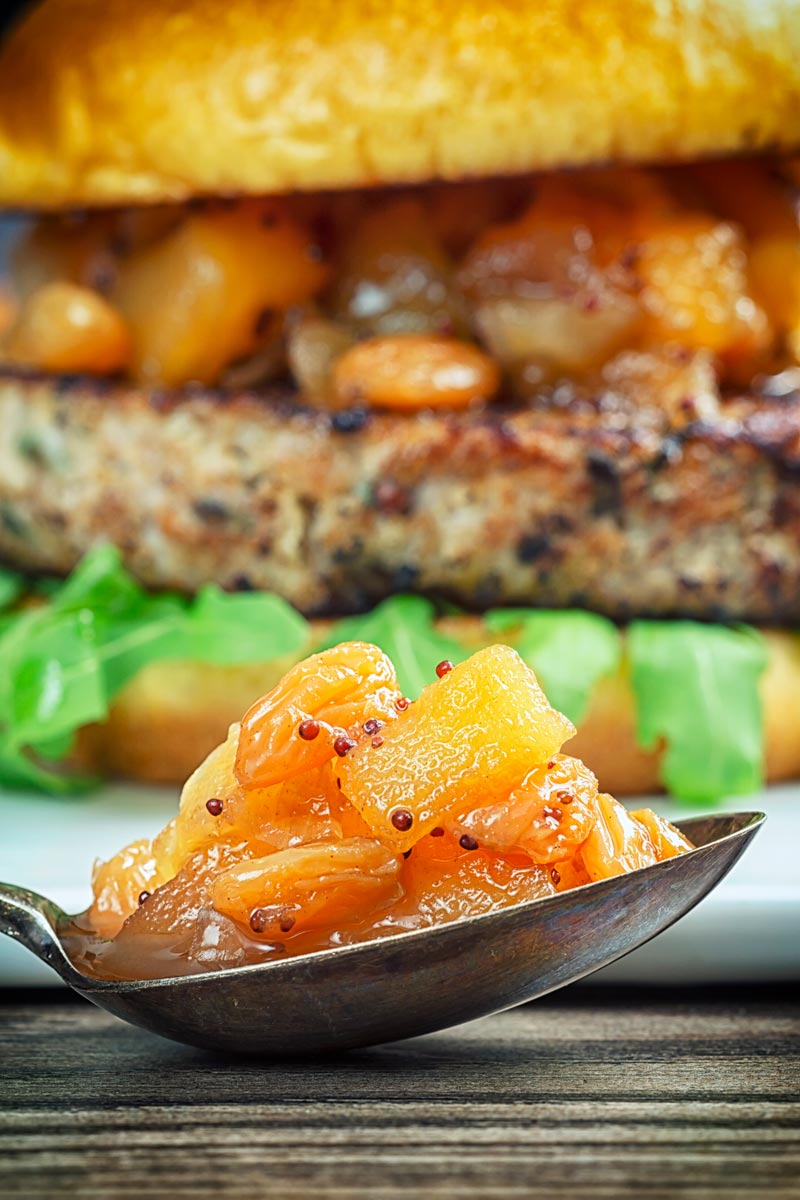 Close up portrait image of a spoonful of chunky apple chutney with an out of focus burger in the background
