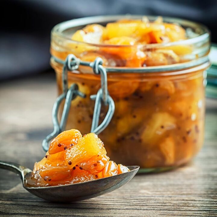 Sqaure image of a spoonful of chunky apple chutney with an out of focus jar of chutney in the background