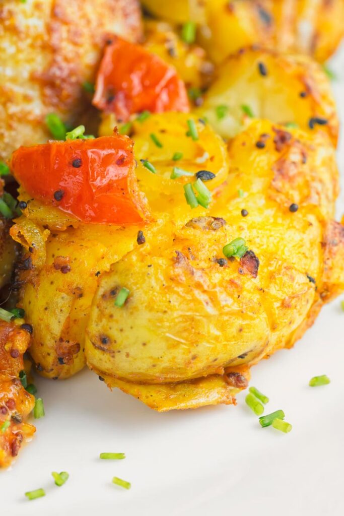 Portrait close up image of lightly crushed Bombay potatoes on a white plate with snipped chives