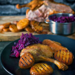 Portrait image of a classic Sunday lunch featuring roast duck, roast potatoes and braised red cabbage