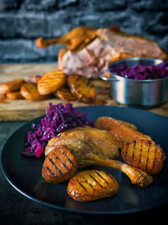 Portrait image of a classic Sunday lunch featuring roast duck, roast potatoes and braised red cabbage