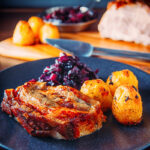 Portrait image of a classic Sunday lunch featuring roast pork, roast potatoes and braised red cabbage