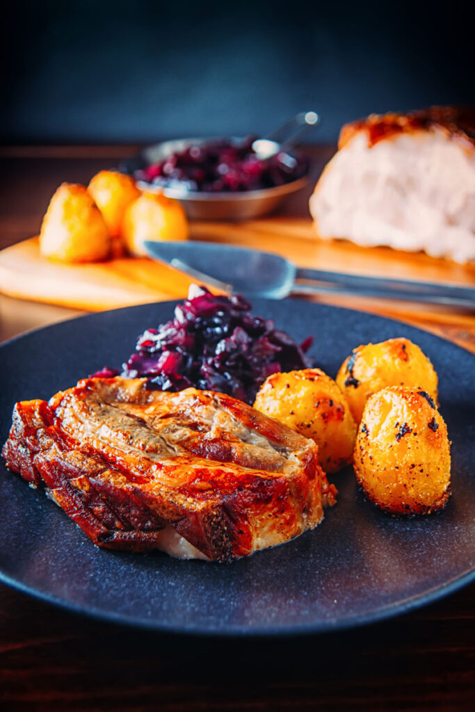 Portrait image of a classic Sunday lunch featuring roast pork, roast potatoes and braised red cabbage