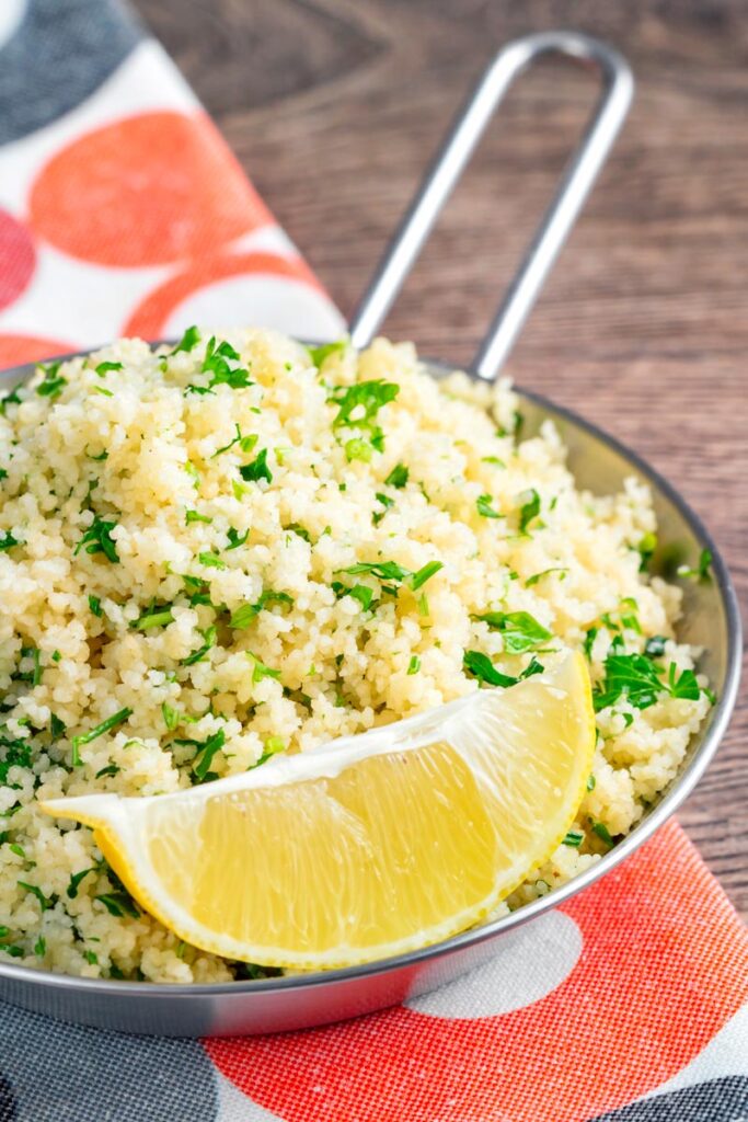 Portrait image of a herby buttered couscous served with a lemon wedge