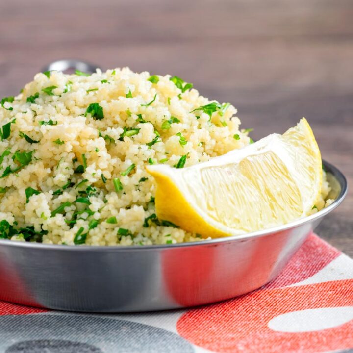 Square image of a herby buttered couscous served with a lemon wedge