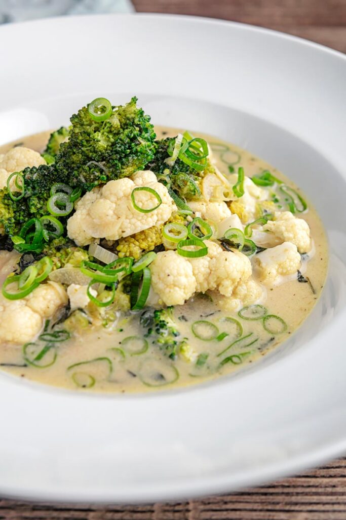 Portrait image of a green Thai curry soup with cauliflower and broccoli served in a white bowl