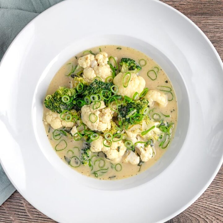 Square overhead image of a green Thai curry soup with cauliflower and broccoli served in a white bowl