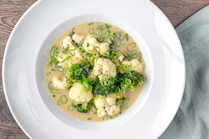 Landscape overhead image of a green Thai curry soup with cauliflower and broccoli served in a white bowl