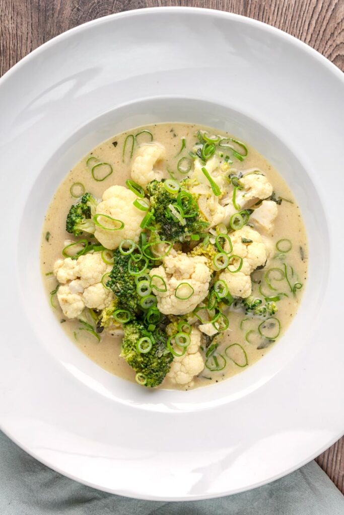 Portrait overhead image of a green Thai curry soup with cauliflower and broccoli served in a white bowl