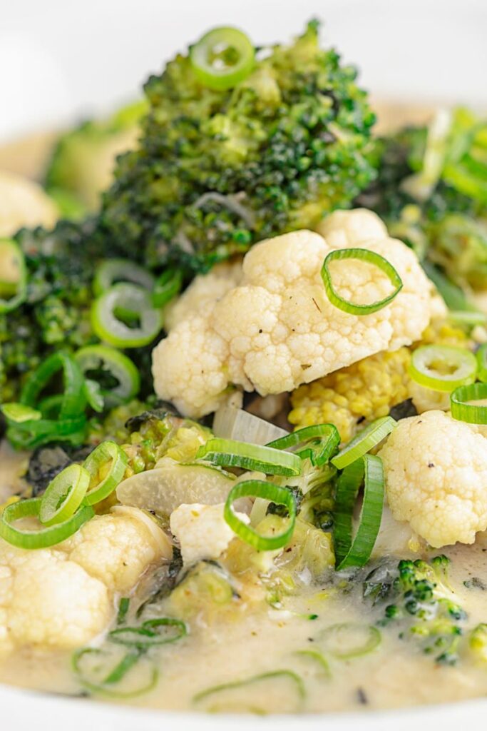 Portrait close up image of a green Thai curry soup with cauliflower and broccoli served in a white bowl