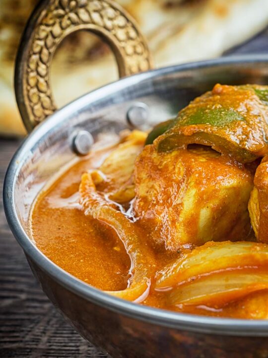 Portrait close up image of a chicken balti curry in a copper coloured curry bowl served with a naan bread