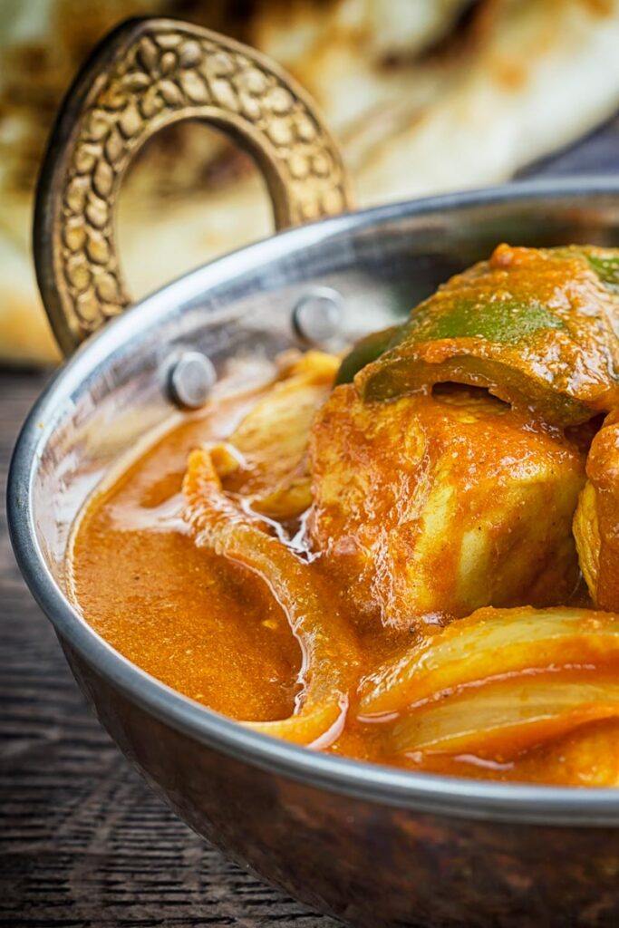 Portrait close up image of a chicken balti curry in a copper coloured curry bowl served with a naan bread