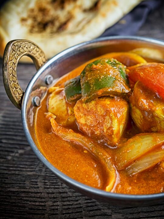 Portrait image of a chicken balti curry in a copper coloured curry bowl served with a naan bread
