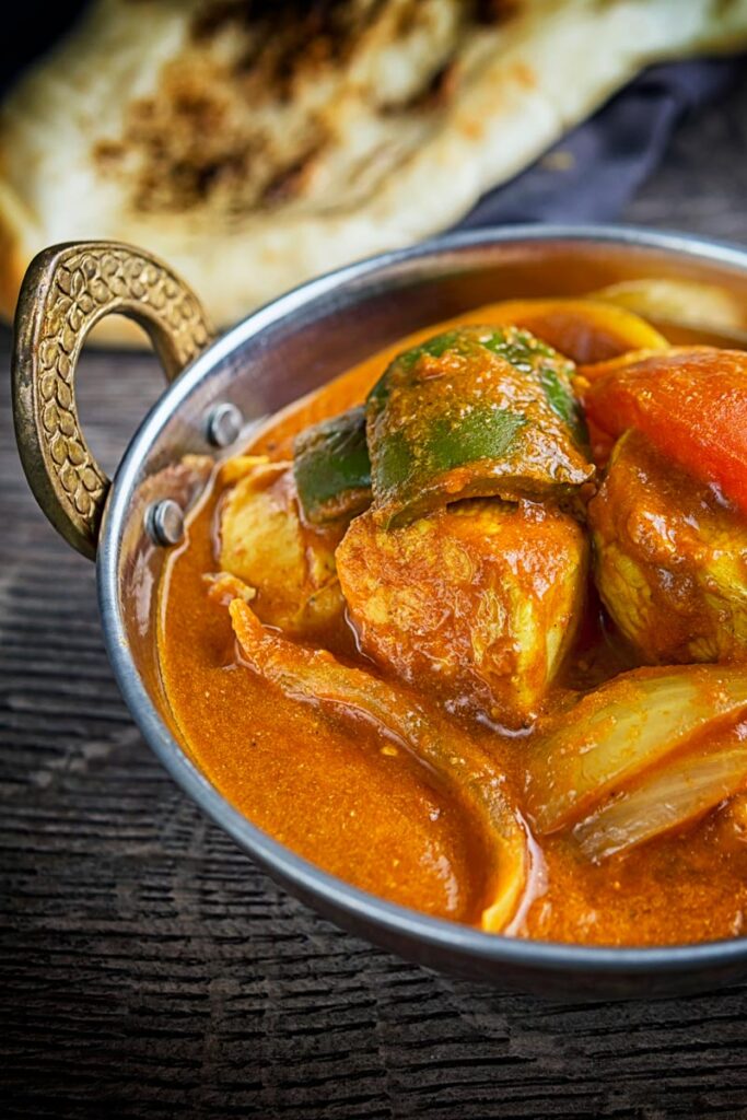 Portrait image of a chicken balti curry in a copper coloured curry bowl served with a naan bread