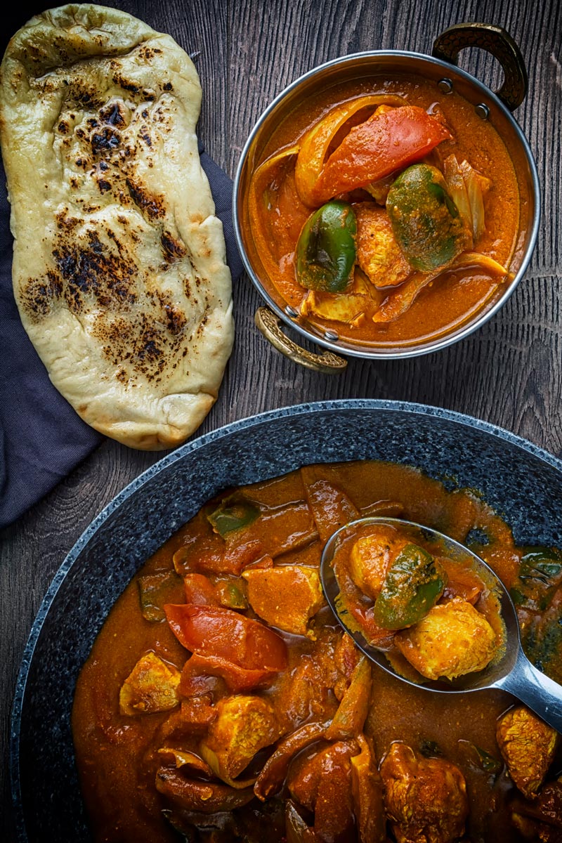 Portrait overhead image of a chicken balti curry in a copper coloured curry bowl served with a naan bread