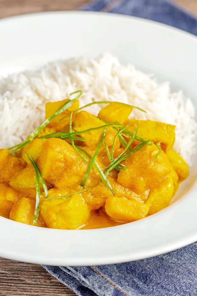Portrait image of a chicken and pineapple curry in a thick sauce with a chiffonade of green chilli and white rice served in a white bowl