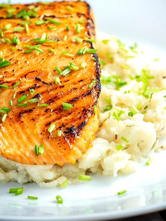 Portrait profile image of honey and soy glazed salmon fillet served on a pile of celeriac mash on a white plate