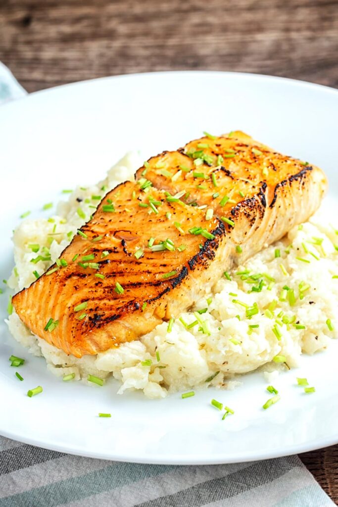 Portrait image of honey and soy glazed salmon fillet served on a pile of celeriac mash on a white plate