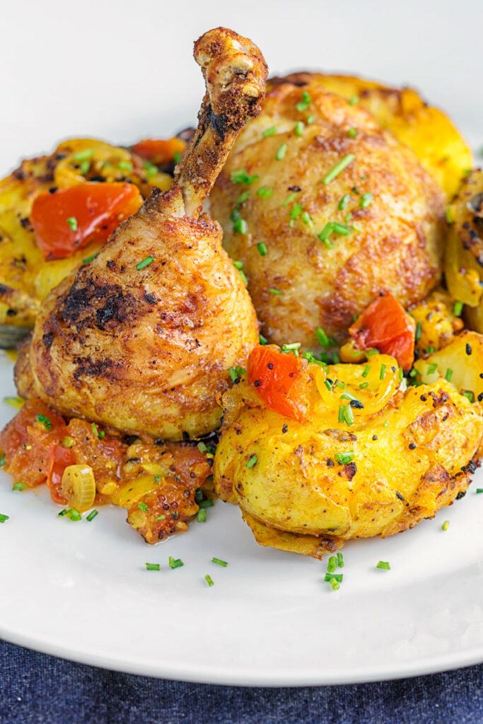 Portrait image of Indian spiced roast chicken legs served with Bombay potatoes on a white plate