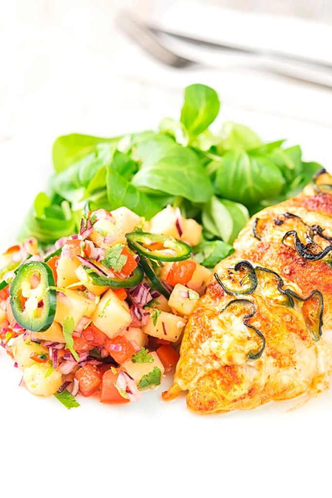 Portrait image of a pineapple salsa served as a side to a chicken breast with green salad