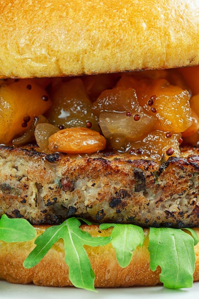 Portrait close up image of a pork and apple burger served on a white rectangle plate with a chutney topping