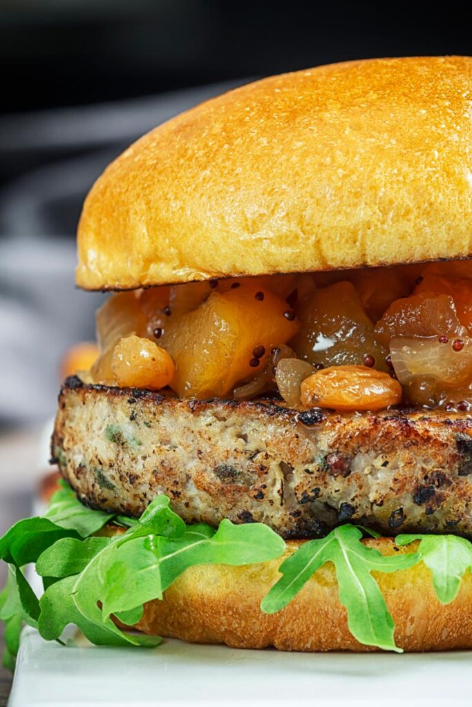 Portrait close up profile image of a pork and apple burger served on a white rectangle plate with a chutney topping