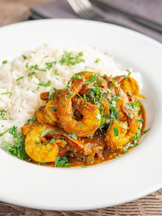 Portrait image of an Indian prawn curry served with white rice and garnished with coriander