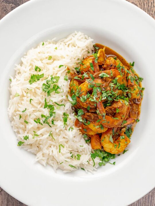 Portrait overhead image of an Indian prawn curry served with white rise and garnished with coriander