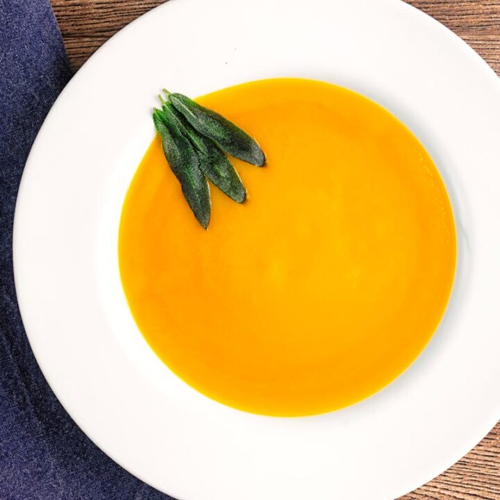 Square overhead image of a bowl of silky roast butternut squash soup served with fried sage leaves