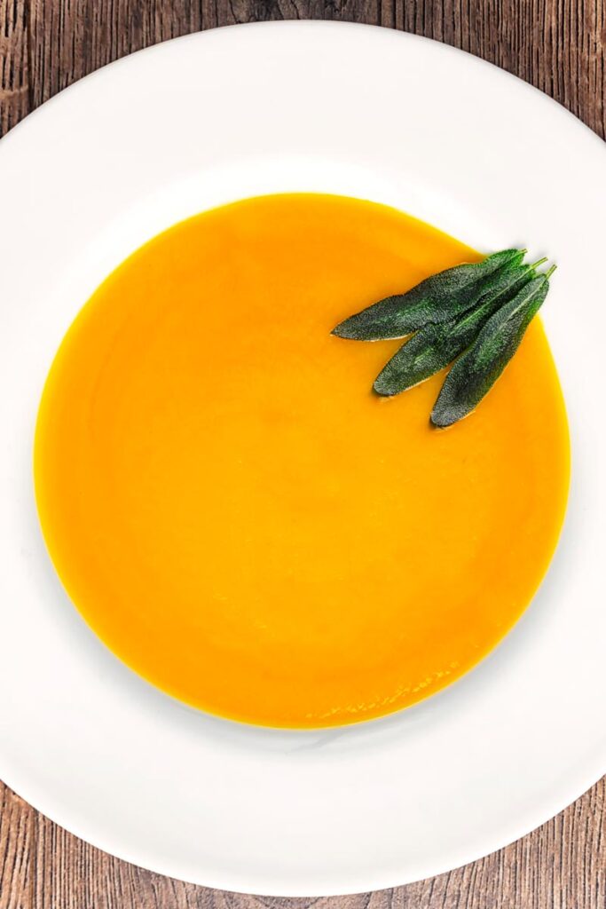 Portrait overhead image of a bowl of silky roast butternut squash soup served with fried sage leaves