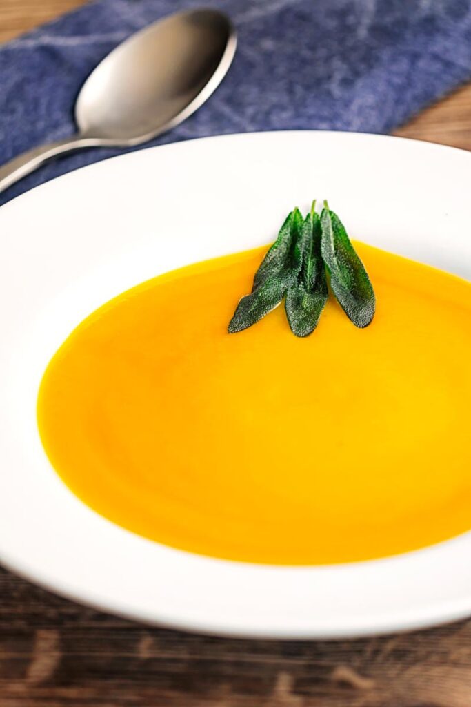 Portrait image of a bowl of silky roast butternut squash soup served with fried sage leaves