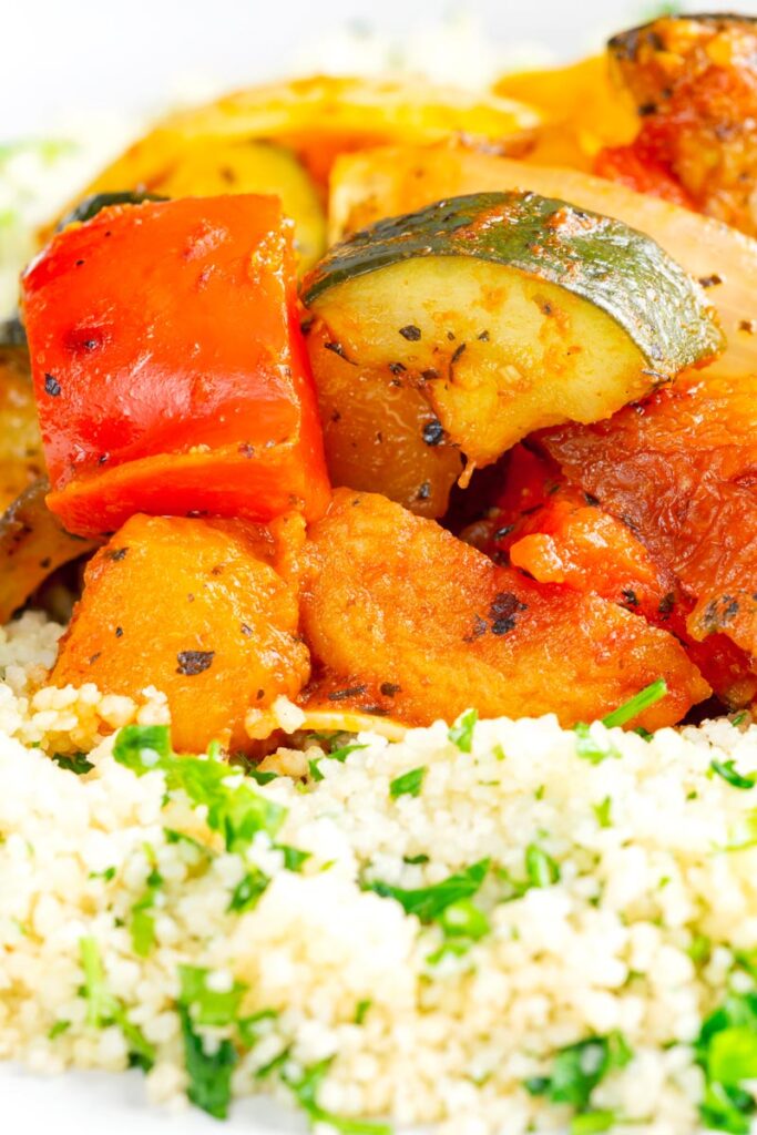 Portrait close up image of a vegetable tagine served on a white plate with herby buttered couscous