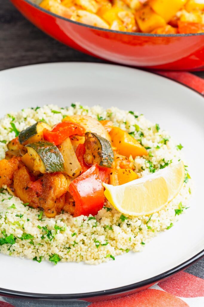Portrait image of a vegetable tagine served on a white plate with herby buttered couscous