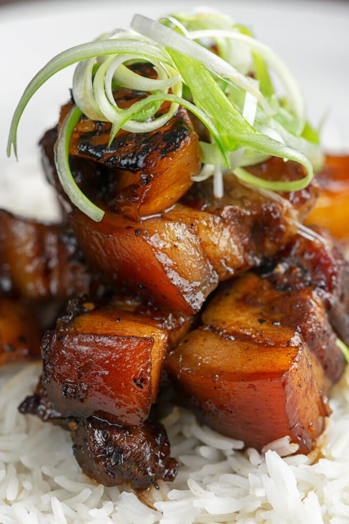 Portrait image of a single serving of glazed sticky pork belly with pineapple on a bed of rice and garnish of shredded green onion