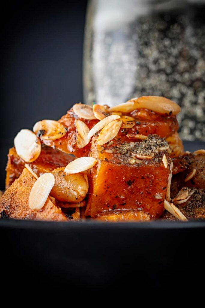 Portrait close up image of a vegetarian sweet potato tagine garnished with flaked almonds and zaatar