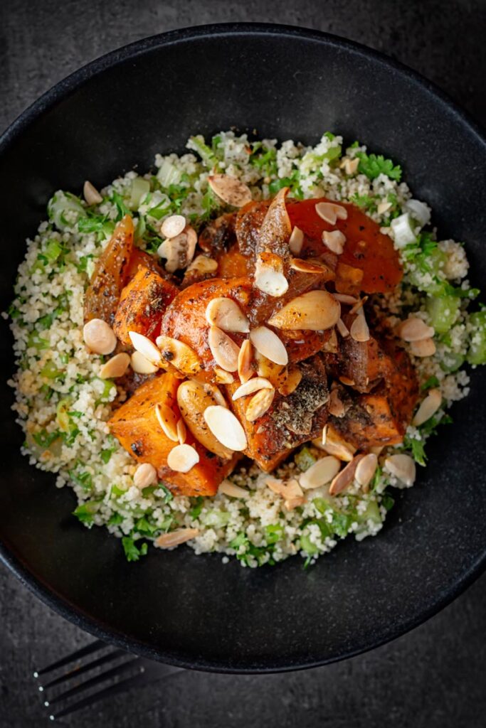 Portrait overhead image of a vegetarian sweet potato tagine garnished with flaked almonds and zaatar on a bed of couscous