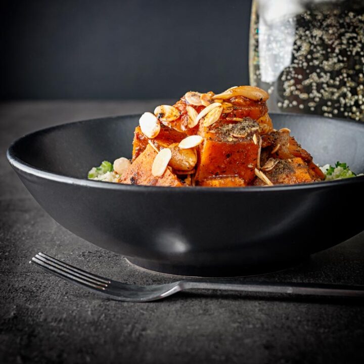 Landscape image of a vegetarian sweet potato tagine garnished with flaked almonds and zaatar