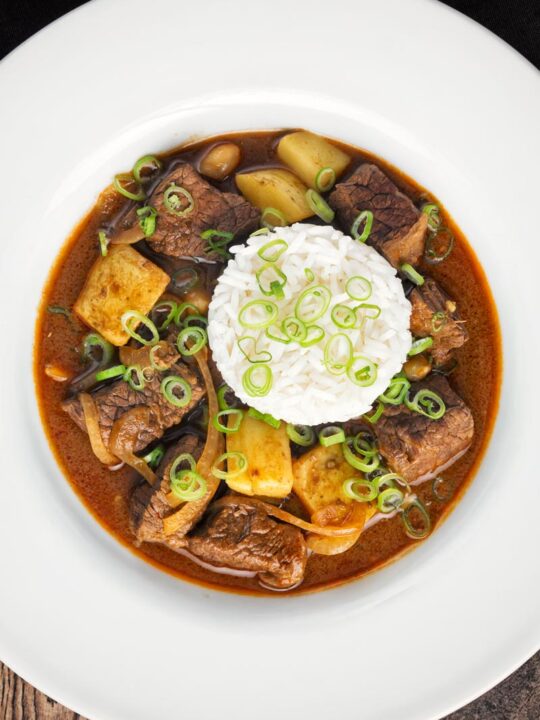 Overhead portrait image of a Thai beef massaman curry served with jasmine rice in a white bowl