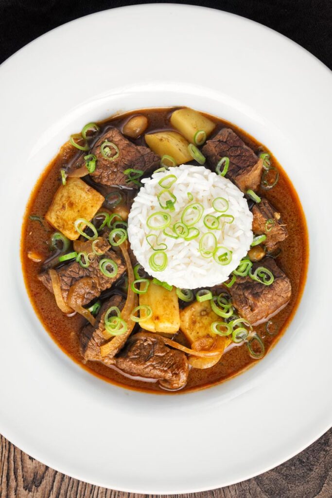 Overhead portrait image of a Thai beef massaman curry served with jasmine rice in a white bowl
