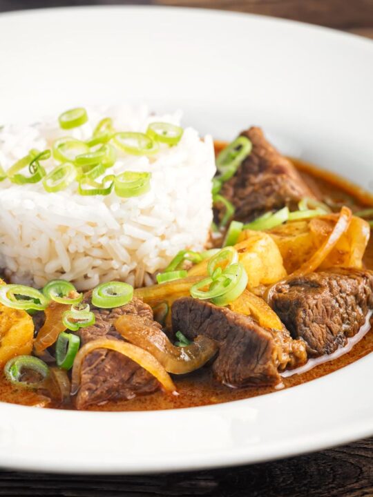 Portrait close up image of a Thai beef massaman curry served with jasmine rice in a white bowl