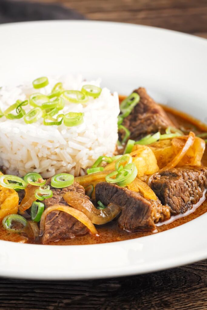 Portrait close up image of a Thai beef massaman curry served with jasmine rice in a white bowl