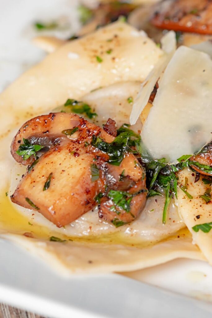 Portrait close up image of mushroom stuffed ravioli with balsamic mushrooms and Parmesan cheese shavings