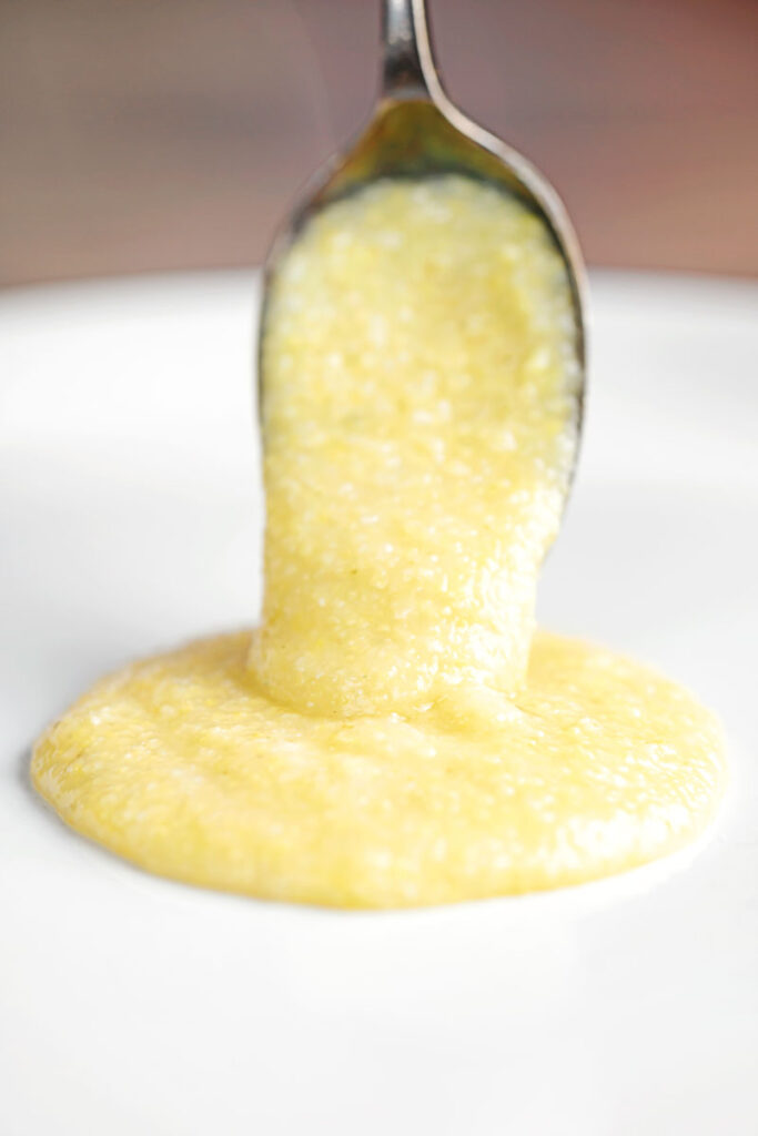 Portrait image of a cheesy polenta porridge being served onto a plate by a spoon