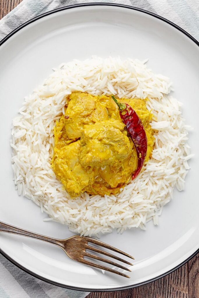 Portrait overhead image of a golden coloured coconut chicken curry served on a bed of Basmati rice with a chilli
