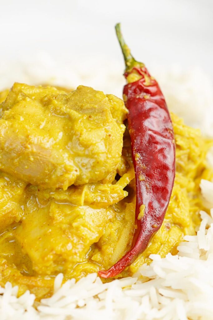 Portrait close up image of a golden coloured coconut chicken curry served on a bed of Basmati rice with a chilli
