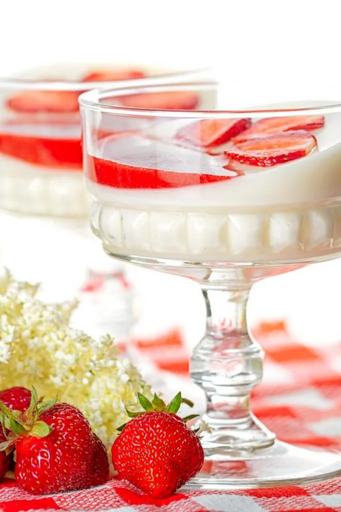 Portrait image of two yoghurt panna cotta served in class bowls with strawberry coulis and strawberry slices