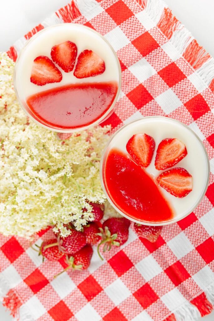 Portrait overhead image of two yoghurt panna cotta served in class bowls with strawberry coulis and strawberry slices